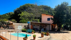 A pool area with a fenced pool, potted plants, and a building with a patio. - Pousada Aracuã - Laguna (Laguna)
