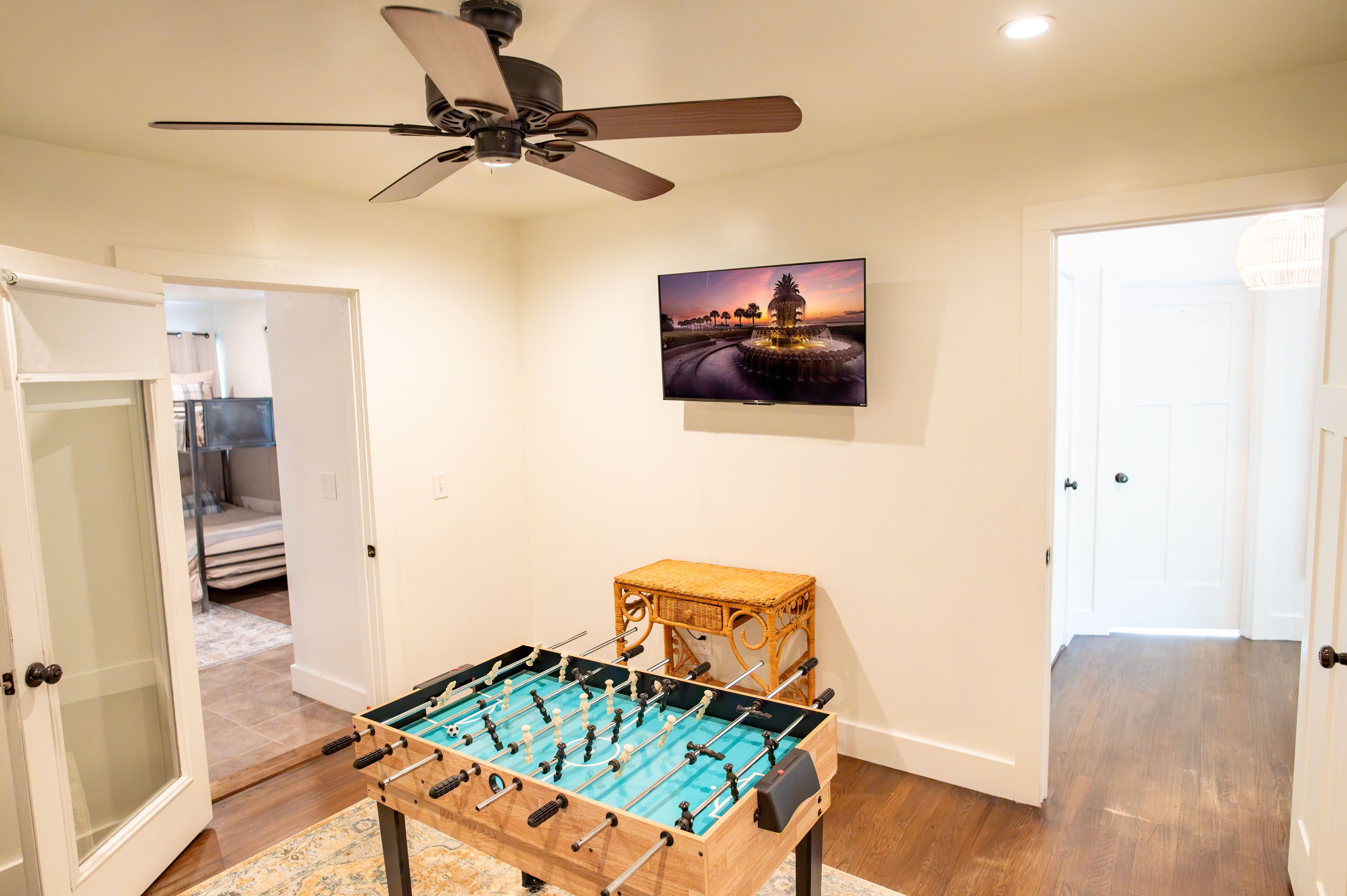 A room with a foosball table, a ceiling fan, and a wall-mounted TV displaying a sunset scene.