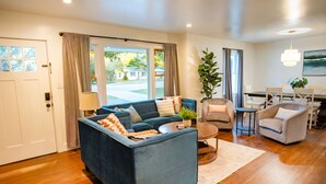 A modern living room with a blue sofa, a round coffee table, and a dining area with a table and chairs. - Creekside Retreat w/ Hot Tub + Game Room, 6 minutes to Downtown, 15 to Folly! (Charleston)