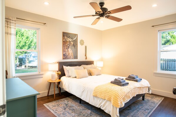 A bedroom with a bed, bedside lamps, a ceiling fan, and a window with curtains. - Creekside Retreat w/ Hot Tub + Game Room, 6 minutes to Downtown, 15 to Folly! (Charleston)