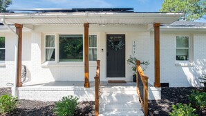 A white brick house with a dark front door, wooden columns, and a covered porch. - Creekside Retreat w/ Hot Tub + Game Room, 6 minutes to Downtown, 15 to Folly! (Charleston)