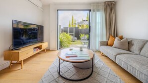 Una sala moderna con televisor de pantalla plana, una mesa redonda, un sofá gris y un ventanal corredizo que da a un patio.