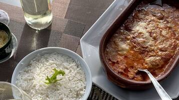 Una mesa con una botella de vino, un cuenco de arroz, un plato de papas fritas y un plato al horno.