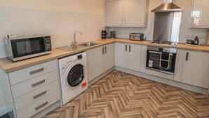 A compact kitchen with a microwave, washing machine, sink, and oven. - The Newborough Apartment 5 (Scarborough)