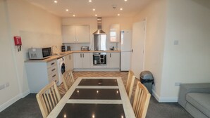 A compact kitchen with a dining table, chairs, and basic appliances. - The Newborough Apartment 5 (Scarborough)
