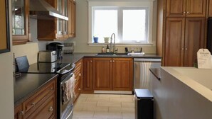 A kitchen with wooden cabinets, a stainless steel sink, and a black trash bin.