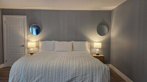 Un dormitorio con cama, dos lámparas de noche, una puerta y dos espejos adosados a la pared.