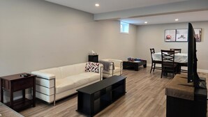 A modern living room with a white sofa, a black coffee table, a small side table, a dining area with a table and chairs, and recessed ceiling lighting.