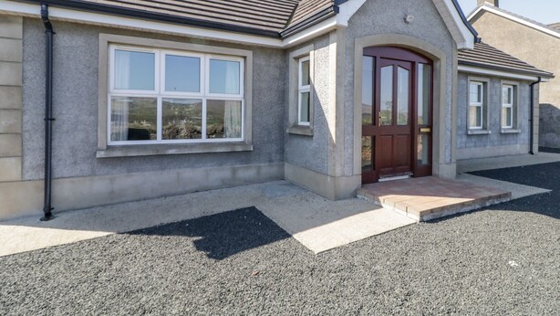 A two-story house with a stone facade, a red door, and a large window. - Mountain View (Ballymoney)