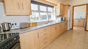 A kitchen with wooden cabinets, a stove, a sink, and a window. - Mountain View (Ballymoney)