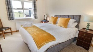 A neatly arranged bedroom with a large bed, a bedside table, a chair, and a window with curtains. - Mountain View (Ballymoney)