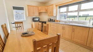 A modern kitchen with wooden cabinets, a dining table, chairs, a microwave, and a window with a view of the outdoors. - Mountain View (Ballymoney)