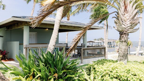 Une propriété située en bord de mer, dotée d’un patio couvert, de palmiers et offrant une vue sur l’océan.