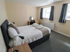 A hotel room with a bed, bedside table, lamp, and a window with curtains.