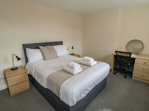 A neatly made bed with white linens, two bedside tables with lamps, a desk with a chair, and a mirror on the wall.