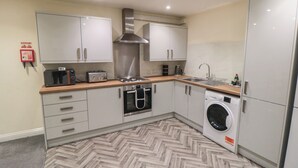 A compact kitchen with a microwave, toaster, stove, oven, sink, and washing machine. - The Newborough Apartment 4 (Scarborough)