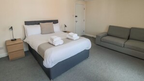 A neatly arranged bedroom with a bed, bedside tables, a sofa, and a door. - The Newborough Apartment 4 (Scarborough)