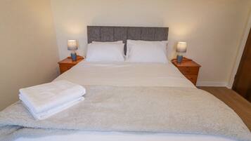 A neatly made bed with white linens, two bedside lamps, and a fluffy white throw blanket.