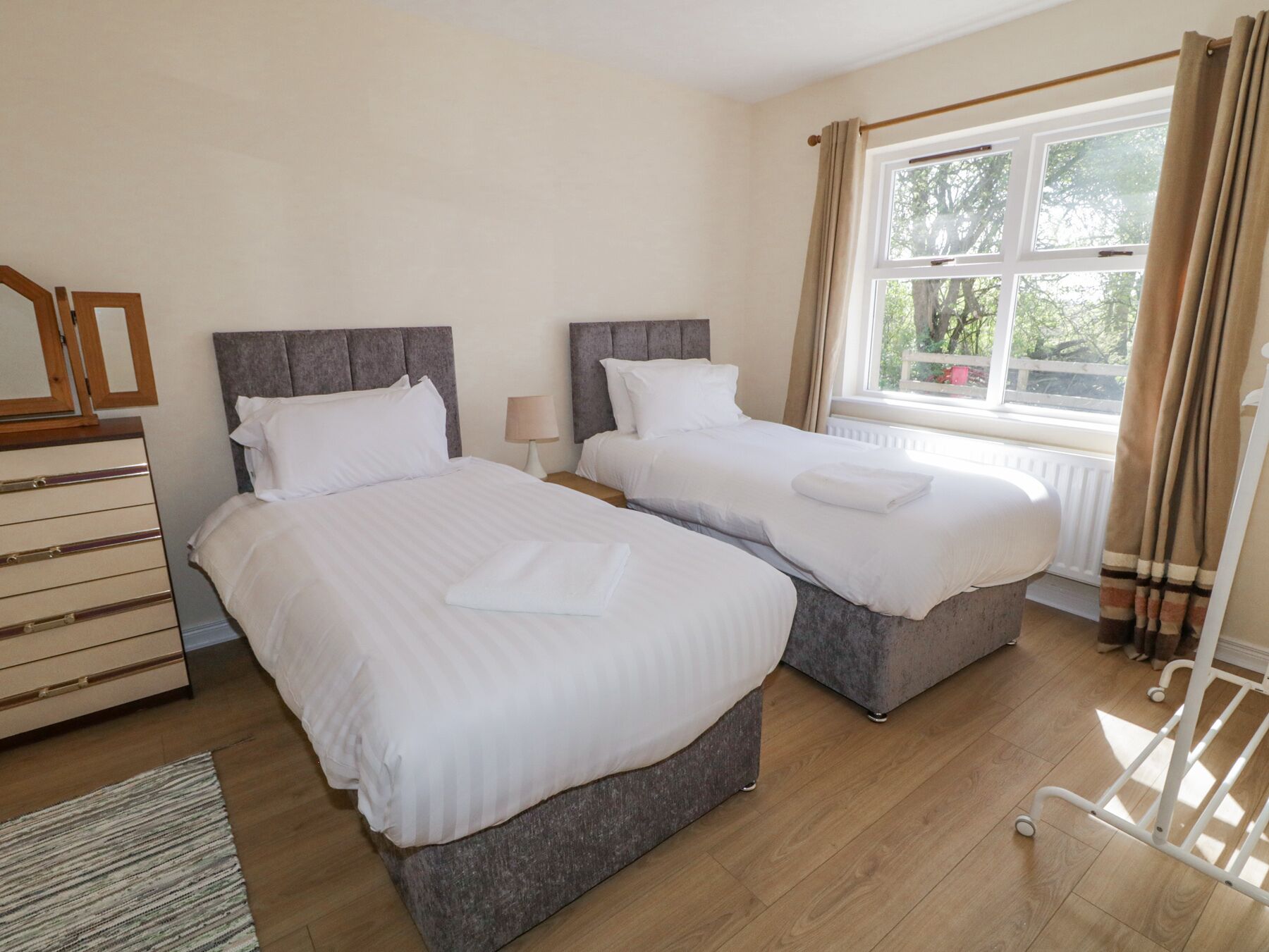 Hotellihuone, jossa on kaksi sänkyä, lipasto, ikkuna verhoilla ja patteri.