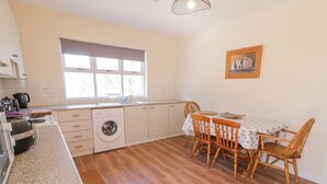 A compact kitchen with a washing machine, a dining table with chairs, and a window providing natural light. - Hill House (Ballymoney)