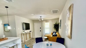 A modern kitchen with a white countertop, bar stools, and a dining area with a round table and blue chairs.