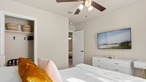A bedroom with a bed, a ceiling fan, a wardrobe, a bedside table, and a wall-mounted TV.