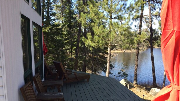 A wooden deck with outdoor seating, overlooking a lake surrounded by trees. - Royal Lake Cabin (Royal Lake)