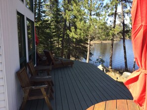 Une terrasse en bois avec des sièges extérieurs, donnant sur un lac entouré d’arbres.