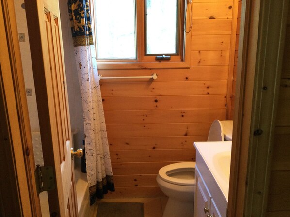 Une petite salle de bain aux murs lambrissés, équipée de toilettes, d’un lavabo et d’une fenêtre.