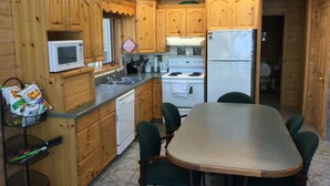 A wooden cabin-style kitchen with wooden cabinets, a white stove, a white refrigerator, a microwave, and a dining table with chairs. - Royal Lake Cabin (Royal Lake)