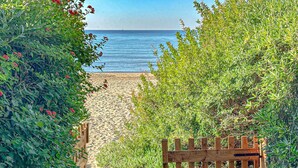 Un cancello di legno conduce a una spiaggia sabbiosa, fiancheggiata da una fitta vegetazione verde.