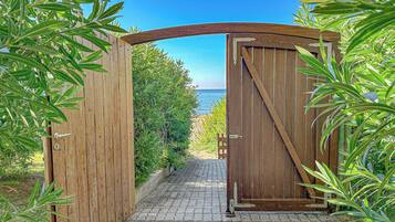 A wooden gate leading to a paved path with a view of the sea.