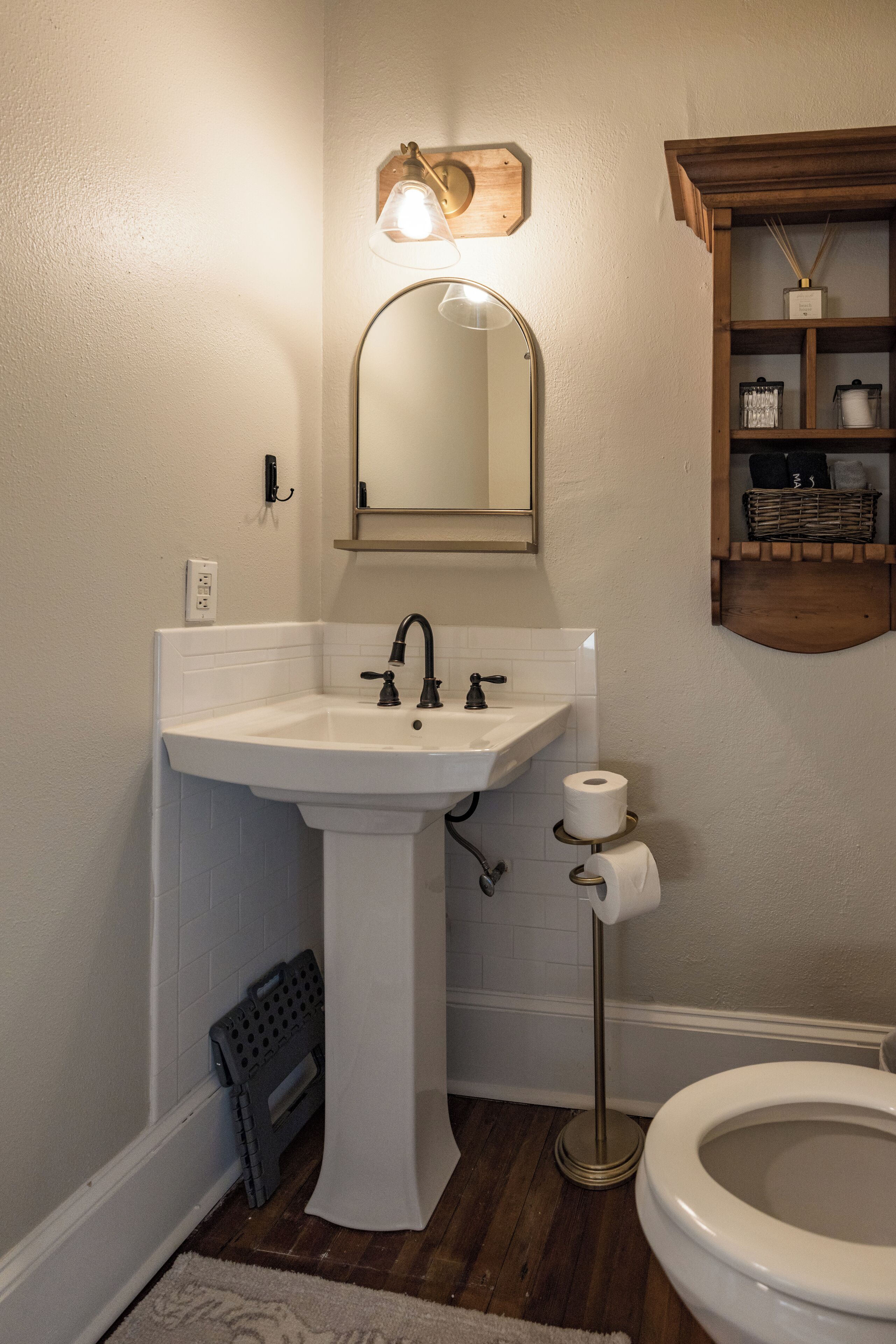 A bathroom with a white sink, a mirror, a toilet, and a shelf with toiletries.
