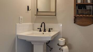 A bathroom with a white sink, a mirror, a toilet, and a shelf with toiletries.
