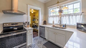 A modern kitchen with a stainless steel range hood, a dishwasher, and a large window with curtains. - The Hansell House, your Downtown Thomasville Destination! Family + Pet Friendly! (Thomasville)
