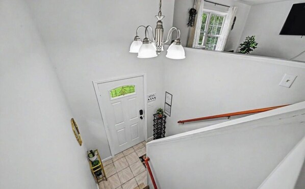 A staircase with a handrail, a door with a green sign, and a chandelier. - Spacious 4-bedroom house in Tobyhanna with game room, firepit (Tobyhanna)