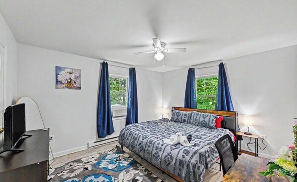 Un dormitorio con cama, escritorio, silla, ventilador de techo y ventana con cortinas.