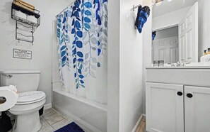 A bathroom with a toilet, a shower curtain with a leaf pattern, a bathtub, a sink with a mirror, and a cabinet. - Spacious 4-bedroom house in Tobyhanna with game room, firepit (Tobyhanna)