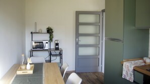 A compact kitchen with a microwave, a small shelf with a plant, and a door with frosted glass panels. - QuickHome Appartamento Gelsomino (Andorno Micca)