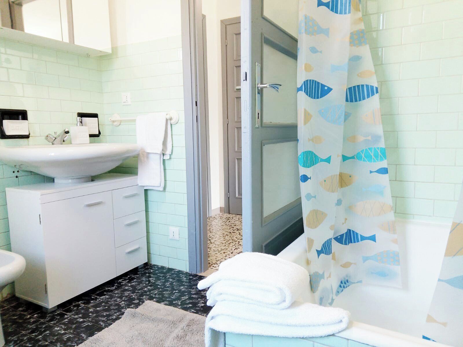 A bathroom with a white sink, a mirror, a toilet, and a shower curtain with fish patterns.