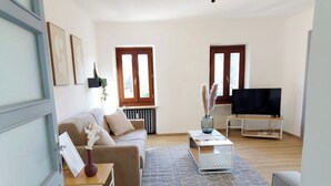 A modern living room with a sofa, coffee table, and TV. - QuickHome Appartamento Gelsomino (Andorno Micca)