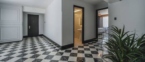 A hallway with a checkered floor, a door leading to a bathroom, and a potted plant.