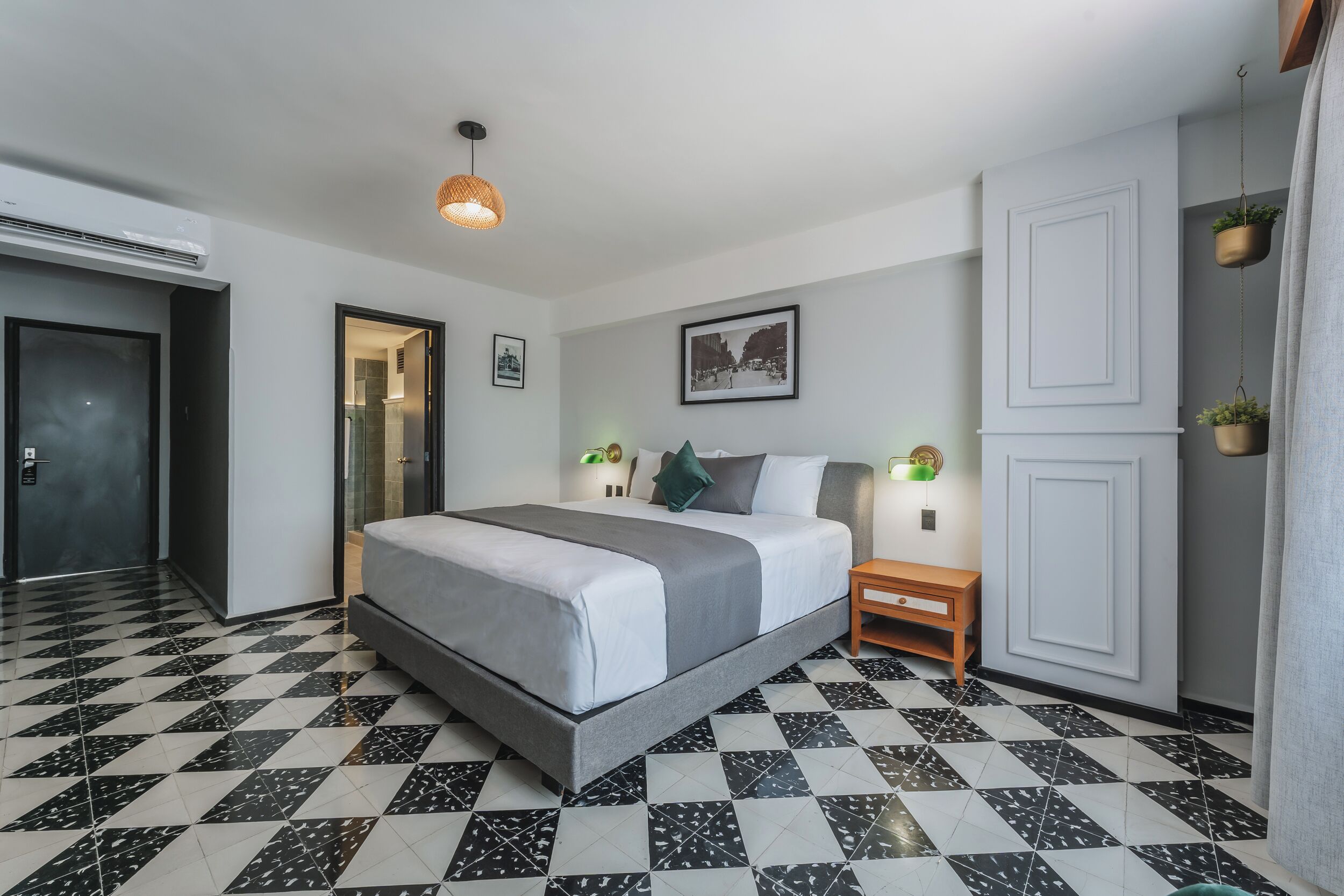 A modern hotel room with a checkered floor, a large bed with grey bedding, two bedside tables with lamps, and a wardrobe.