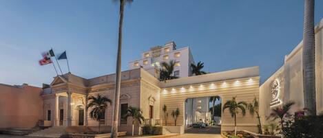 A hotel with a grand entrance, palm trees, and flags.