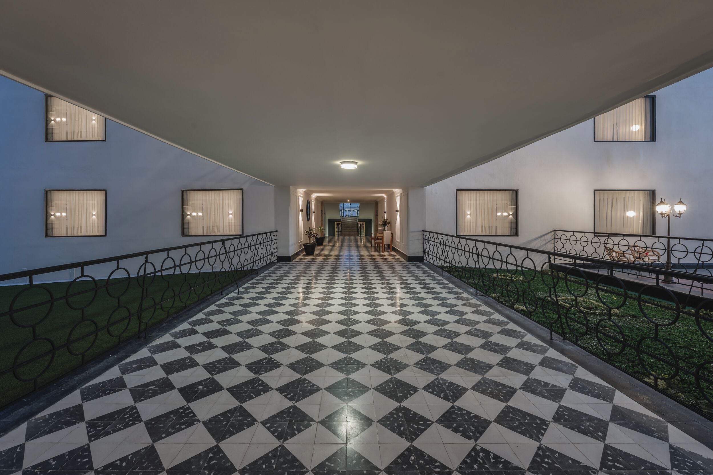 Un suelo a cuadros que conduce a una escalera con barandilla y vista de un edificio al fondo.