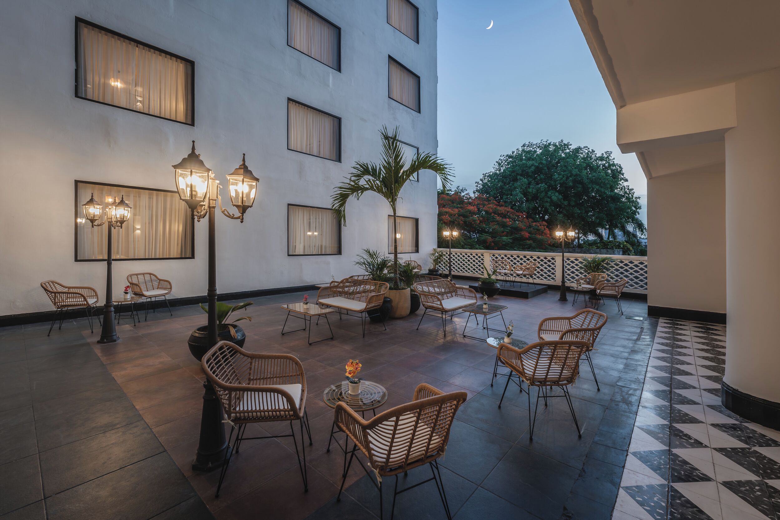 A hotel patio with wicker furniture, potted plants, and wall-mounted lights.