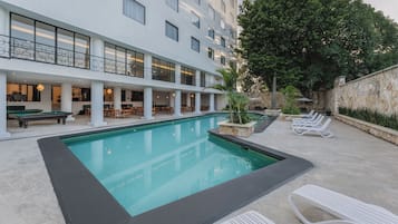 A pool area with lounge chairs, a pool, and a building with multiple floors and balconies.