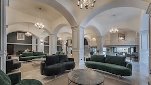 Eine großzügige Lobby mit hohen Gewölbedecken, grünen gepolsterten Sofas und einem zentralen Marmortisch.
