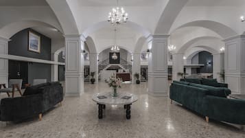 A spacious lobby with a marble floor, two sofas, a central table with a vase, and a chandelier.