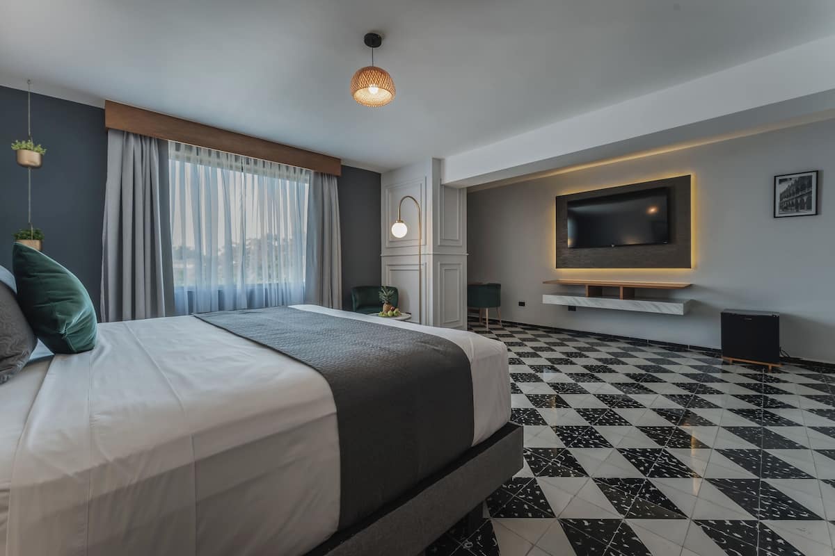 Ein modernes Hotelzimmer mit einem großen Bett, einem flachbildfernseher an der Wand, einem Schachbrettfußboden und Blick auf die Stadt durch das Fenster.